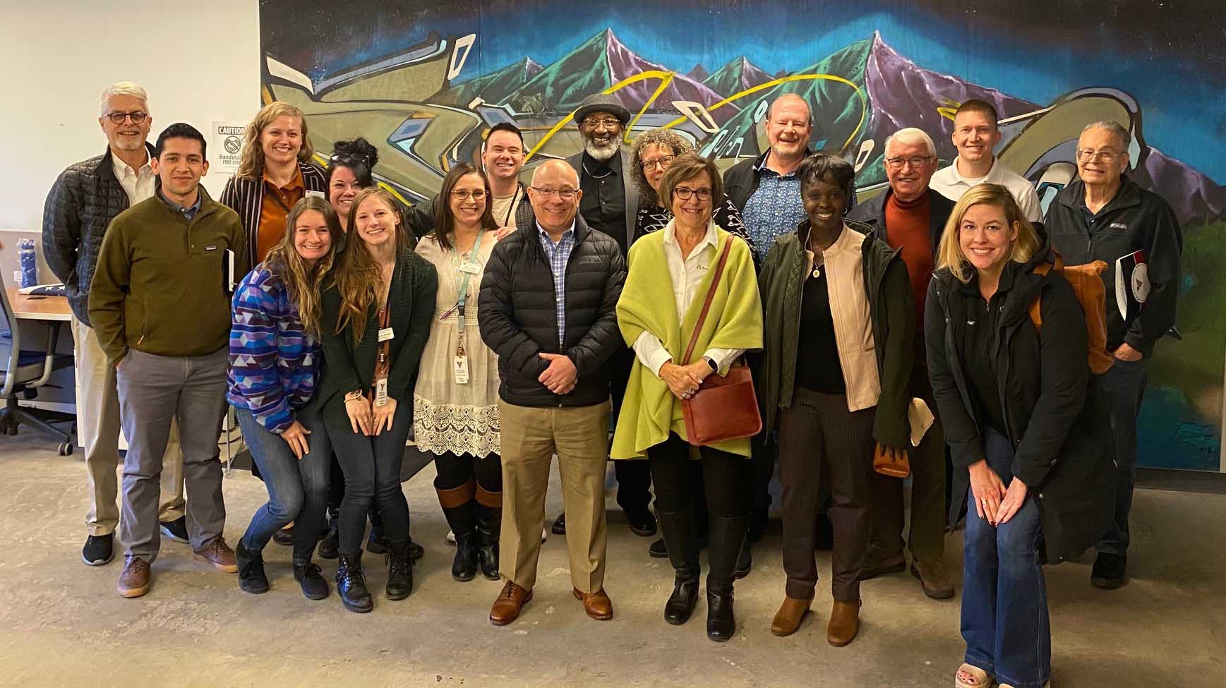 Group of eighteen adults in front of a mountain mural at the VOA in Denver